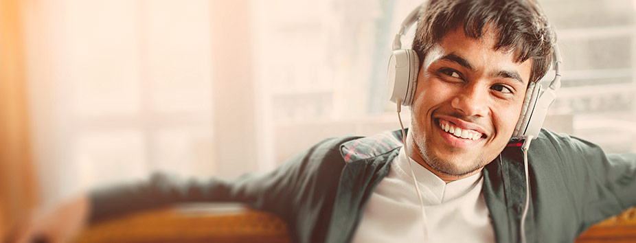 A young man is smiling and sitting on a couch, with headphones on.